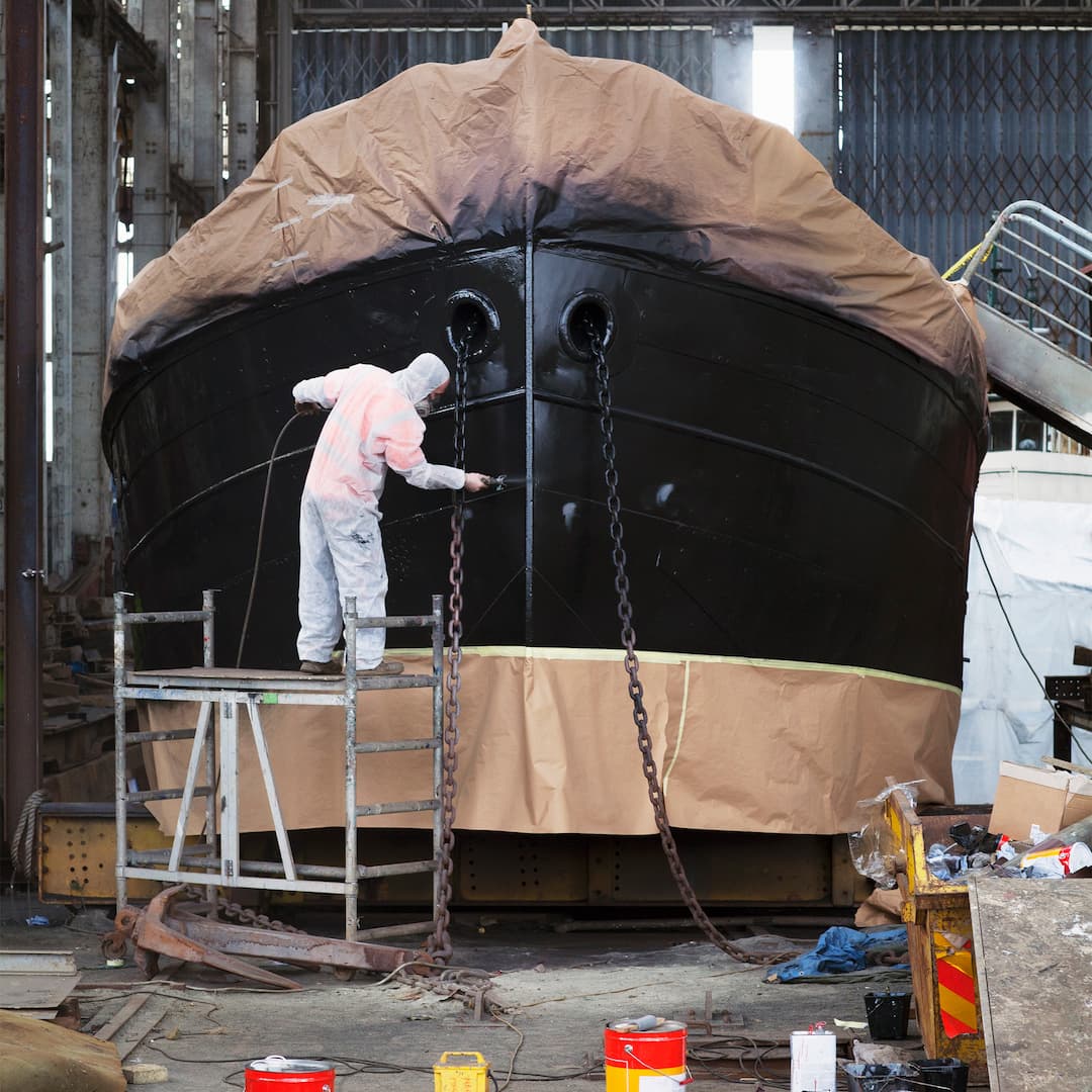 Worker on top of scaffolding painting boat in ship