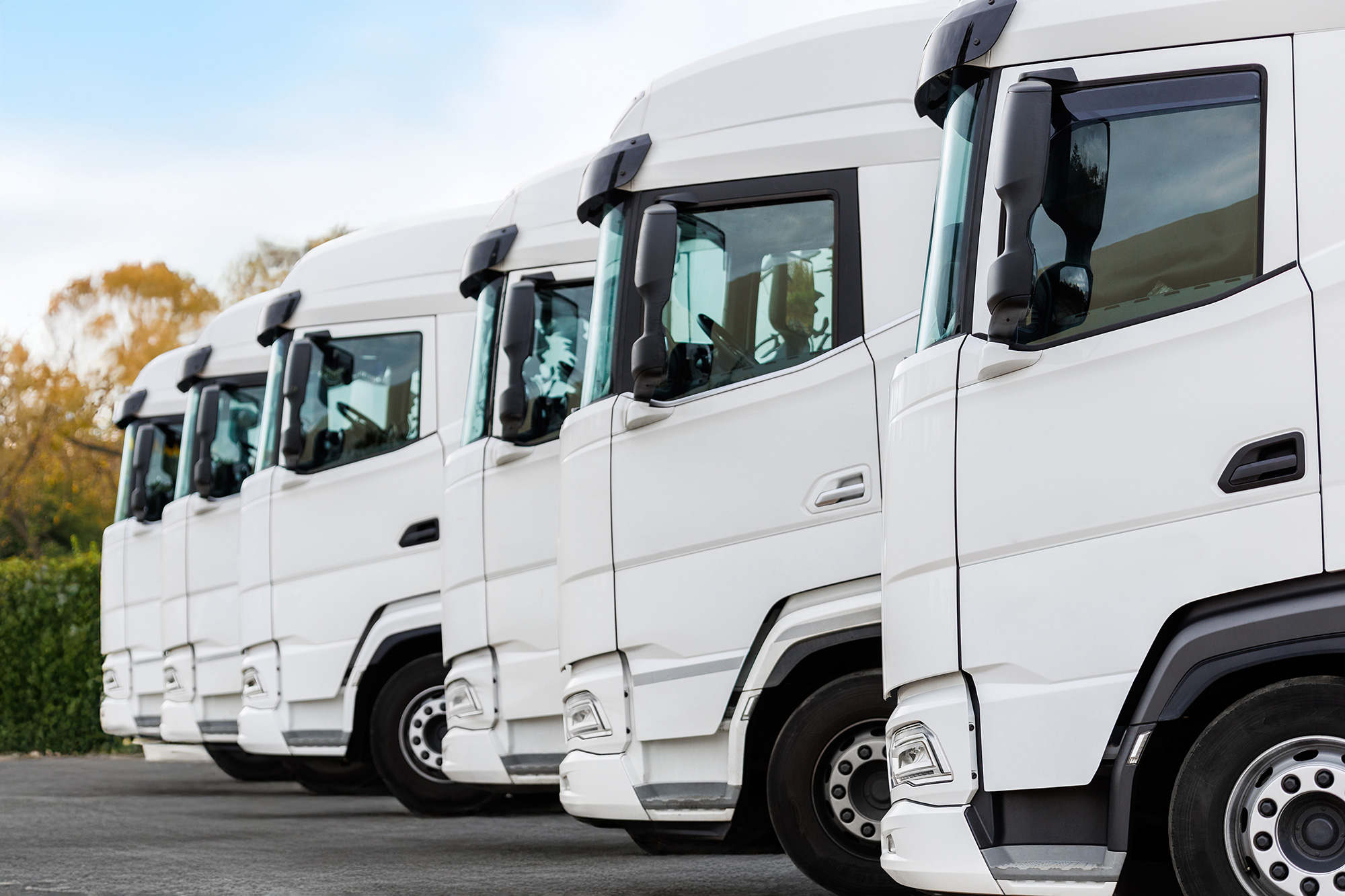 Fleet of new modern electric hybrid hydrogen or diesel white trucks parked in line row outdoors. Cargo freight industrial tra